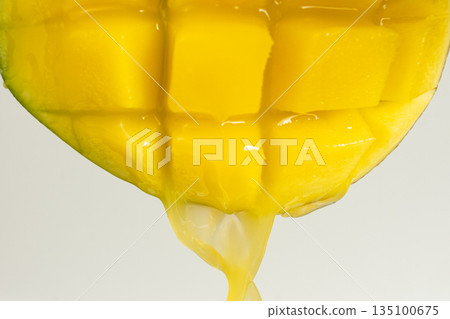 Macro of mango juice dripping from sliced fruit cubes Macro of mango juice dripping from sliced fruit cubes 135100675