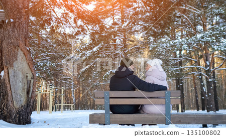 Pair Enjoying Evening On Snowy Woodland Bench, Two People Sharing Tender Moment Amid Winter Forest Landscape, Couple Seated On Bench Surrounded By Snow And Tall Pine Trees During Sunset Pair Enjoying Evening On Snowy Woodland Bench, Two People Sharing Tender Moment Amid Winter Forest Landscape, Couple Seated On Bench Surrounded By Snow And Tall Pine Trees During Sunset 135100802