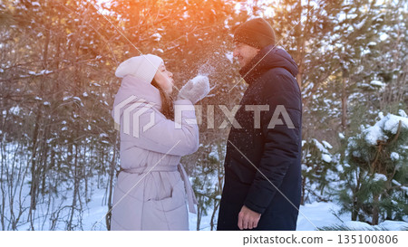 Playful Snowball Game In Sunny Woodland, Couple Enjoys Cheerful Winter Fun Amidst Sunlit Pine Trees, Cheerful Woman Playfully Hurls Snow At Her Partner In Bright Pine Forest Setting 135100806