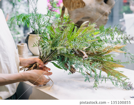 A natural green arrangement made from bundles of leaves and branches indoors A natural green arrangement made from bundles of leaves and branches indoors 135100855