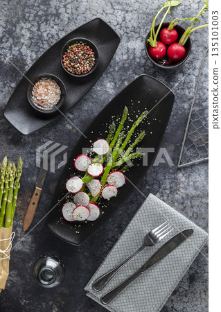 Fresh asparagus and sliced radishes on black plate 135101003
