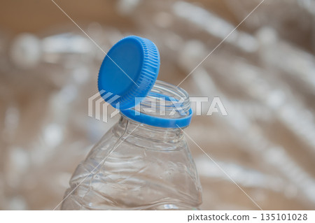 Water bottle cap is off and resting on top of an empty plastic bottle near crumpled plastic Water bottle cap is off and resting on top of an empty plastic bottle near crumpled plastic 135101028