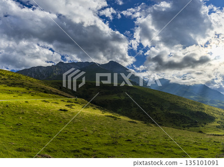 Green Pyrenees mountains with sun rays breaking through clouds 135101091