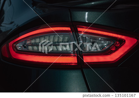 Close-up of a glowing red car taillight at night with visible light streaks Close-up of a glowing red car taillight at night with visible light streaks 135101167