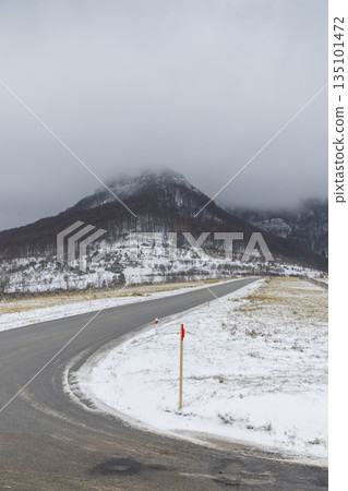 Winding road through snowy mountain landscape with fog Winding road through snowy mountain landscape with fog 135101472