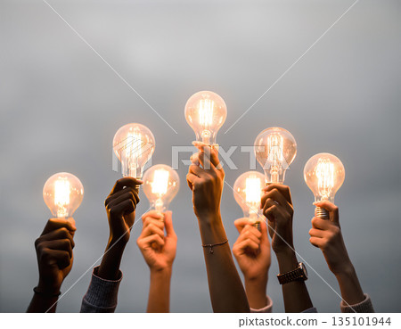 Hands hold light bulbs against a grey sky during an outdoor event in the evening Hands hold light bulbs against a grey sky during an outdoor event in the evening 135101944