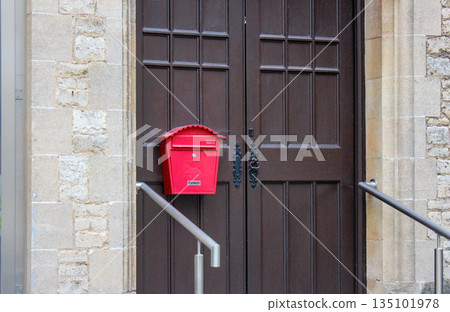 Oxford, United Kingdom - Dec 22, 2025: Red mailbox on a large wooden door of an old building. 135101978