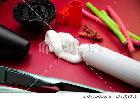 Close-up side view on a pink background, hairdryer with attachments, stylers and curling irons for straightening and creating curls, foam for volume and long-lasting, curlers in different shapes and 135102011