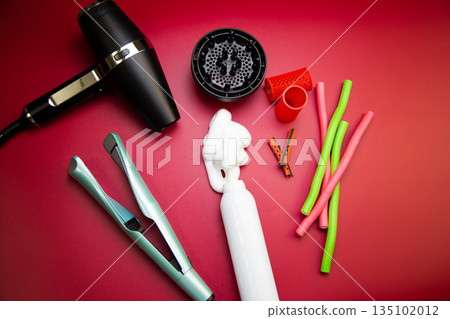 Top view on a pink background, a hairdryer with attachments, stylers and curling irons for straightening and creating curls, foam for creating volume and long-term holding, curlers of different shapes 135102012