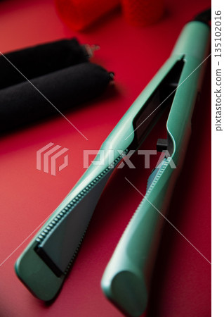 In the foreground is a curling iron loi creating curls against the background of curlers in outfocus on a pink background. The concept of hair care, hairstyle, hairdressing. High quality photo In the foreground is a curling iron loi creating curls against the background of curlers in outfocus on a pink background. The concept of hair care, hairstyle, hairdressing. High quality photo 135102016