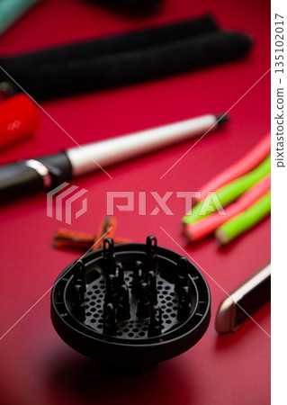 In the foreground is a diffuser for creating curls and hair volume against the background of curlers and irons in out-of-focus on a pink background. The concept of hair care, hairstyle, hairdressing 135102017