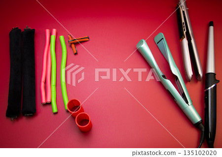 On the side there are stylers and curling irons for straightening and creating curls, on the other side there are curlers of different shapes and sizes on a pink background with space for text. The 135102020