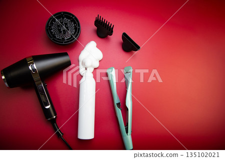 Top view of hair styling foam in a white bottle, surrounded by a hairdryer and hair dryer attachments and a curling iron on a pink background with space for text. The concept of long-term hair styling 135102021