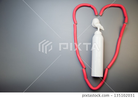 On the side, on a gray background, there is a bottle of foam for long-term hair styling, white foam poured out of it, around it pink bendable curlers form a heart with space for text. The concept of On the side, on a gray background, there is a bottle of foam for long-term hair styling, white foam poured out of it, around it pink bendable curlers form a heart with space for text. The concept of 135102031