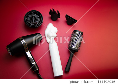 Top view of the hair styling foam in a white bottle on a pink background, surrounded by nozzles for drying hair, a hair dryer and a round styling comb. The concept of long-term hair styling, creating Top view of the hair styling foam in a white bottle on a pink background, surrounded by nozzles for drying hair, a hair dryer and a round styling comb. The concept of long-term hair styling, creating 135102036