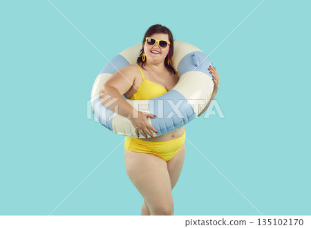 Fat woman in rubber ring wearing swimsuit looking at camera on blue background. 135102170