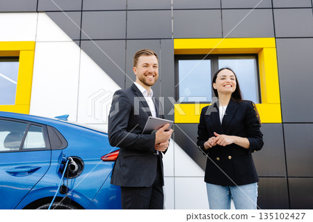 Happy female client standing at brand new car and taking keys from dealer in dealership outdoor. The woman is very happy with the new car, holding the keys in her hands Happy female client standing at brand new car and taking keys from dealer in dealership outdoor. The woman is very happy with the new car, holding the keys in her hands 135102427