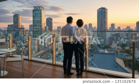 Back view of a couple looking at the city night view from the terrace of a high-rise apartment building 135102678