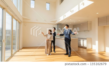一對夫婦和一位房地產經紀人正在參觀一棟明亮的新房子，房子有一個開放式天花板。 135102679