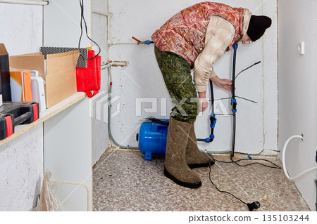 Homeowner secures heating cable to incoming house pipe with plastic ties in unheated utility room of rural house. 135103244