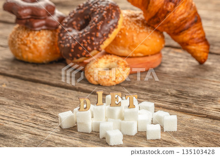 Diet concept with sugar cubes and pastries on rustic wooden table Diet concept with sugar cubes and pastries on rustic wooden table 135103428