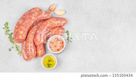 Raw sausages with olive oil, garlic, thyme and salt on light stone background with copy space, top view 135103434