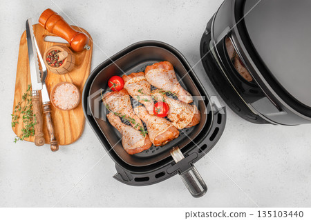 Raw chicken drumsticks seasoned with herbs in air fryer basket on light kitchen background, top view Raw chicken drumsticks seasoned with herbs in air fryer basket on light kitchen background, top view 135103440