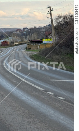 Wet Country Road Heading Into Village With Weathered Markings And Surrounding Natural Features Wet Country Road Heading Into Village With Weathered Markings And Surrounding Natural Features 135103472