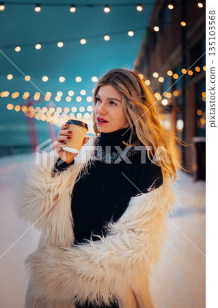 Woman holding coffee cup under string lights in winter evening Woman holding coffee cup under string lights in winter evening 135103568