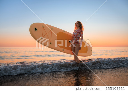 Young woman standing on beach with paddle sup boards during summer vacation 135103631