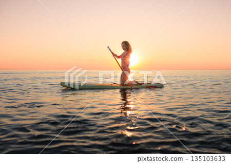 Young woman walking on stand up paddle sup boards by the sea during summer vacation 135103633