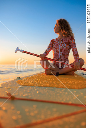 Young woman sitting on stand up paddle sup boards by the sea during summer vacation 135103635