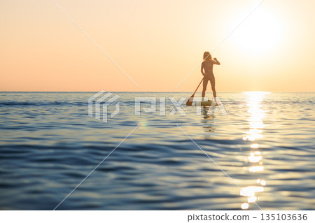Young woman walking on stand up paddle sup boards by the sea during summer vacation Young woman walking on stand up paddle sup boards by the sea during summer vacation 135103636