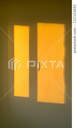 Golden shadow of a window cast on a wall during sunset, creating a warm and minimalist interior scene. Golden shadow of a window cast on a wall during sunset, creating a warm and minimalist interior scene. 135103691