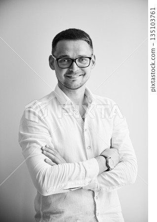 Charming man smiling straight to camera. Portrait of handsome young male in casual clothes keeping arms crossed while standing on white background. Black and white image. 135103761