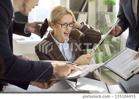 Stressed businesswoman overwhelmed by paperwork and phones during office deadline Stressed businesswoman overwhelmed by paperwork and phones during office deadline 135104455