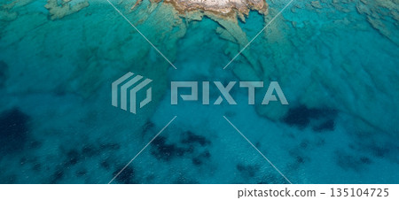 Aerial view of crystal clear turquoise water gently washing a rocky shore Aerial view of crystal clear turquoise water gently washing a rocky shore 135104725