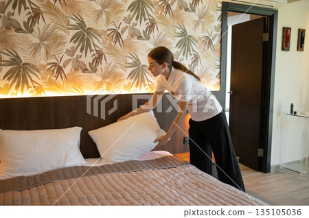 Young woman in hotel uniform doing bed in a hotel room 135105036