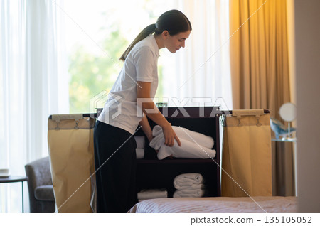 Young girl in hotel service uniform changing linen in a hotel suit Young girl in hotel service uniform changing linen in a hotel suit 135105052