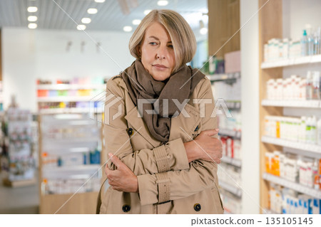 Mature caucasian woman feeling sick and shivering in the drug store Mature caucasian woman feeling sick and shivering in the drug store 135105145