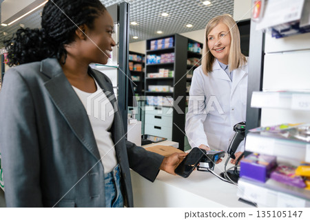 Smiling female customer paying at the cashier desk at the drug store 135105147