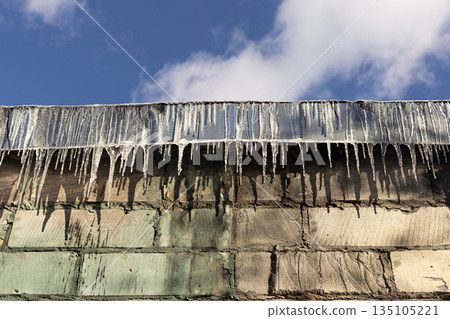 Icicles hanging from the roof edge of a residential house in winter weather 135105221