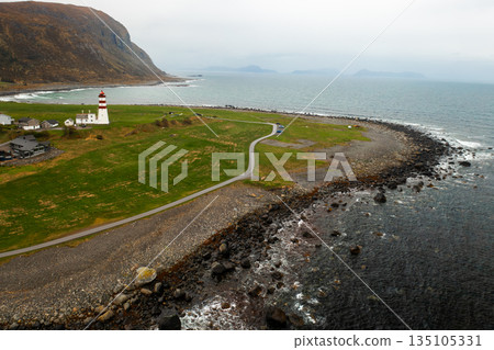 Lighthouse on a green grassy hill with sea and mountains along the Norwegian coastline. Lighthouse on a green grassy hill with sea and mountains along the Norwegian coastline. 135105331