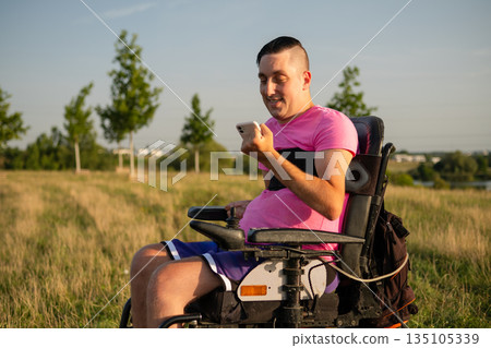 : Outdoor lifestyle scene of a wheelchair user holding a smartphone under bright sunlight. : Outdoor lifestyle scene of a wheelchair user holding a smartphone under bright sunlight. 135105339
