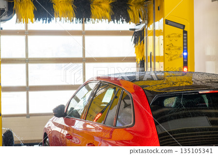 Red automobile being washed in a modern automatic car wash facility. Red automobile being washed in a modern automatic car wash facility. 135105341
