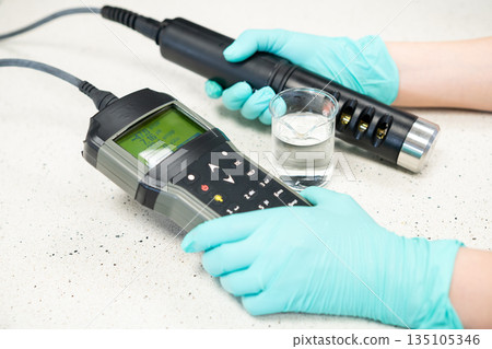 Female hands in protective gloves measuring water pH with a field pH meter. Female hands in protective gloves measuring water pH with a field pH meter. 135105346