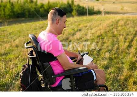 Inclusive lifestyle concept showing a wheelchair user enjoying digital content on a tablet in nature. Inclusive lifestyle concept showing a wheelchair user enjoying digital content on a tablet in nature. 135105354