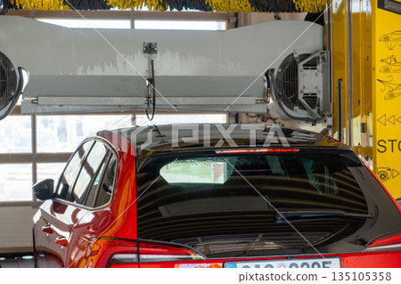 Red car passing through an automatic car wash, water and brushes cleaning the vehicle. Red car passing through an automatic car wash, water and brushes cleaning the vehicle. 135105358