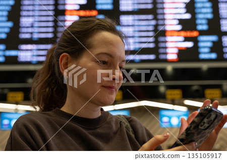 Woman using smartphone and checking flight schedule at airport Woman using smartphone and checking flight schedule at airport 135105917