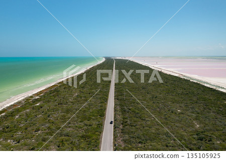 Car driving on a scenic road between turquoise sea and pink salt evaporation ponds in Rio Lagartos, Yucatan, Mexico Car driving on a scenic road between turquoise sea and pink salt evaporation ponds in Rio Lagartos, Yucatan, Mexico 135105925